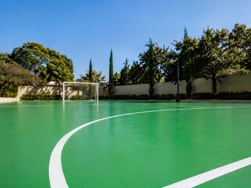 Quadra de futsal externa pintada com Tinta PU verde tráfego RAL 6024 e linhas brancas, sob céu azul